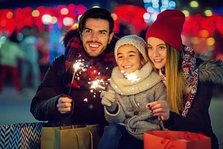 Young, happy couple is hugging their daughter and holding fireworks at Christmas